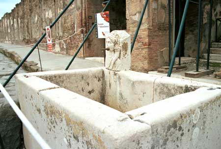 A well on a main street made of marble with a carved head spitting the water.